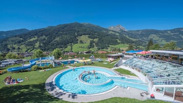 Ein Schwimmbecken mit kreisförmigem Design, umgeben von einer Rasenfläche und einem Gebäude mit Glasfassade.