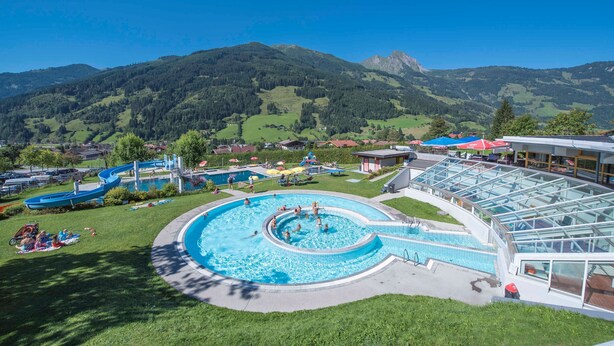 A swimming pool with a circular design, surrounded by a grassy area and a building with a glass facade.