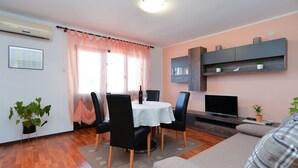 A modern living room with a dining area, a flat-screen TV, and a sofa.