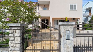 A modern two-story building with a gated entrance, stone pillars, and a staircase leading to the entrance.