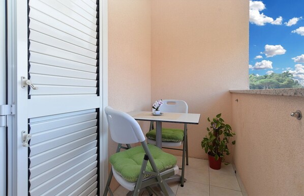 A small balcony with a table and chairs, a potted plant, and a door with blinds.