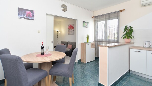 Eine moderne Küche mit Essbereich, ausgestattet mit einem runden Holztisch, grauen Stühlen, einer kleinen Schrank und einem Topf mit Pflanze.