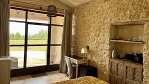 A room with a large window, a bed, a desk, and a stone wall. - La Verrière, Très Jolie Chambre Indépendante Avec Courette Abritée (Bonnieux)