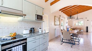 Una cocina moderna con encimeras de granito, horno empotrado y microondas. Cuenta con un comedor con mesa y sillas, y vistas al exterior a través de amplias ventanas.