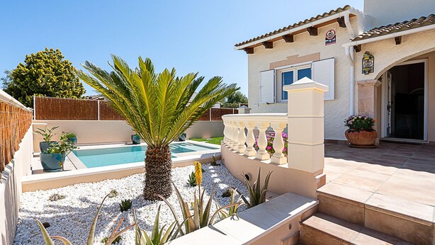 Una piscina rodeada de guijarros blancos, una palmera y un edificio con techo de tejas y un balcón.