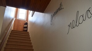 A staircase with a wooden handrail and carpeted steps leading to a landing. The landing has a textured wall with the words "yours" and "relax" written on it. - Cozy Home Near Sea and Arago Market, 2-Star Comfort (Les Sables-d'Olonne)