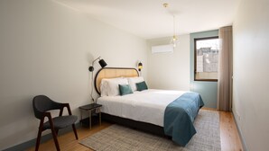 Een slaapkamer met een bed, een stoel, een nachtkastje, een lamp en een raam met gordijnen.