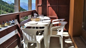 A balcony with a table set for two, overlooking a mountainous landscape. - Cozy 2-Room Apartment for 6 with Balcony, Near Slopes, Pet-Friendly (Risoul)