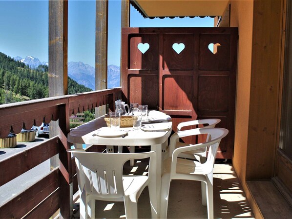 A balcony with a table set for two, overlooking a mountainous landscape.