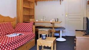 A cozy room with a wooden bed, a small table with a mug, a shelf with baskets, and a television on a cabinet. - Cozy 2-Room Apartment for 6 with Balcony, Near Slopes, Pet-Friendly (Risoul)