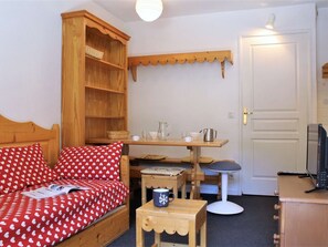Um quarto aconchegante com uma cama de madeira, uma mesa pequena com uma caneca, uma estante com cestos e uma televisão em um armário.
