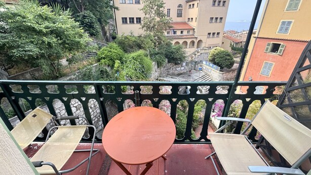Un balcón con dos sillas y una mesita, con vista a un patio con edificios y árboles.