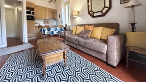 Una sala de estar con sofá, mesa de centro, alfombra estampada y un comedor con mesa y sillas.