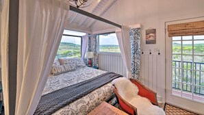 A bedroom with a large bed, a chair, a chandelier, and a view of the outdoors. - Spacious Getaway ~ 12 Acres, Views, & Hot Tub! (Strawn)