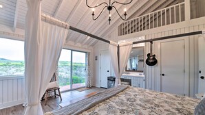 A bedroom with a large bed, a chandelier, a view of the outdoors, and a sliding door leading to a balcony. - Spacious Getaway ~ 12 Acres, Views, & Hot Tub! (Strawn)
