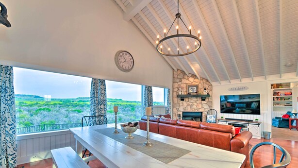 A spacious living area with a large window, a stone fireplace, a television, and a cozy seating area. - Spacious Getaway ~ 12 Acres, Views, & Hot Tub! (Strawn)