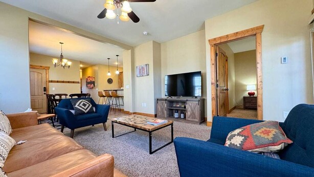A living room with a brown leather sofa, a blue armchair, a coffee table, and a TV. There is a wooden door leading to another room.