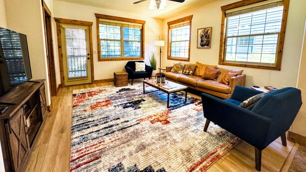 A spacious living room with a ceiling fan, a leather sofa, a blue armchair, and a coffee table. - Mountain Chic Condo Near Grand Targhee and Driggs (Driggs)