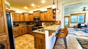 A kitchen with wooden cabinets, a microwave, and a bar area with stools. - Mountain Chic Condo Near Grand Targhee and Driggs (Driggs)