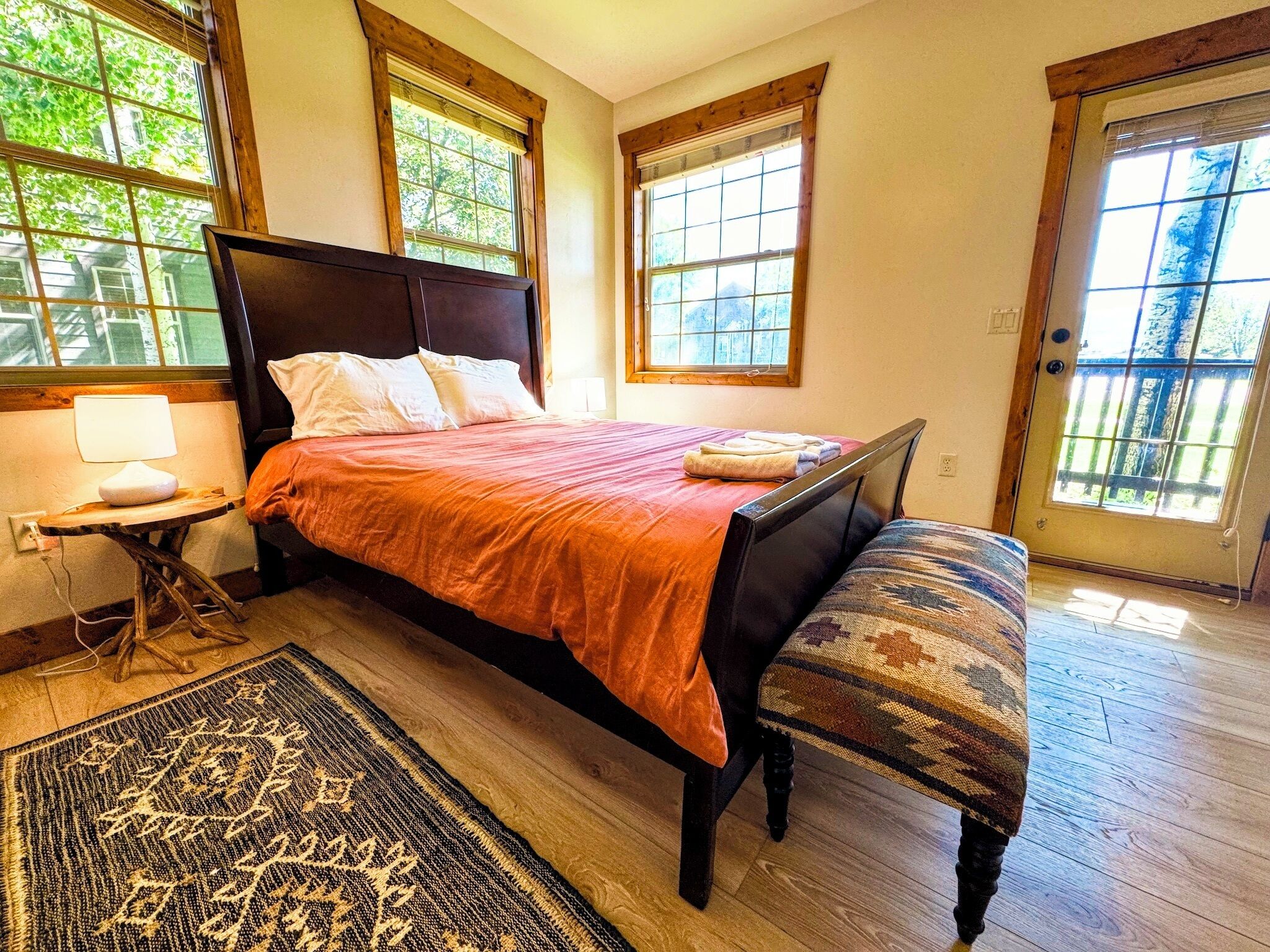 A bedroom with a bed, a bench, a rug, and a nightstand.