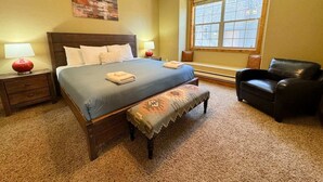 A bedroom with a large bed, a bench, a chair, and a window.