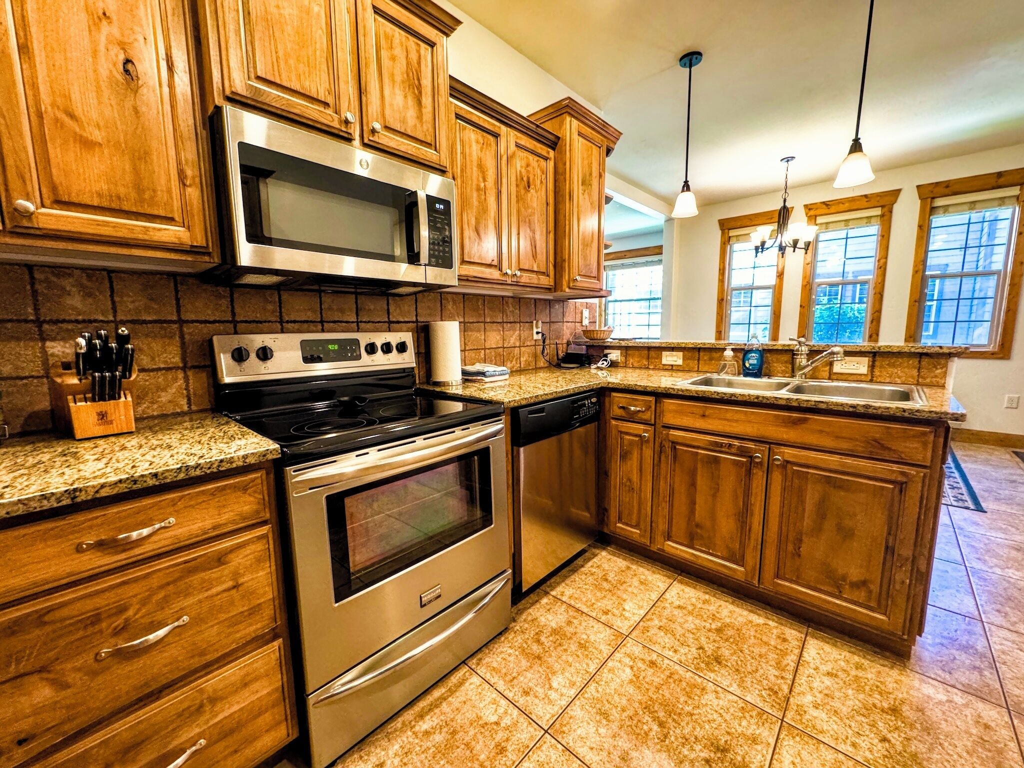 A kitchen with wooden cabinets, stainless steel appliances, granite countertops, and a window with a view.