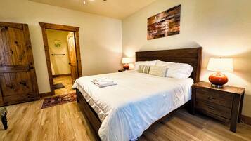 Ein Schlafzimmer mit Holzboden, einem Bett mit weißer Bettwäsche, einem Holz-Kopfteil, zwei Nachttischen mit Lampen und einem Deckenventilator.