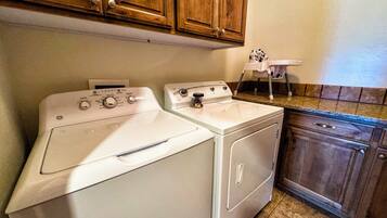 A laundry area with a front-loading washer and dryer, wooden cabinets above, and a small chair.