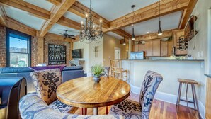 A cozy dining area with a wooden table and patterned chairs, a chandelier, and a view of a brick wall with a sign.