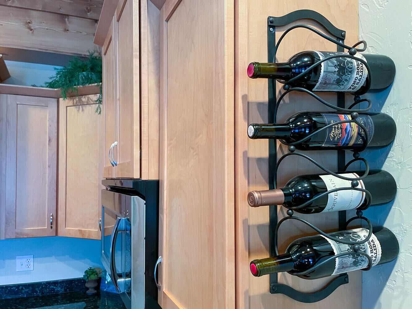 A kitchen with wooden cabinets, a stainless steel oven, and a wine rack holding four bottles.