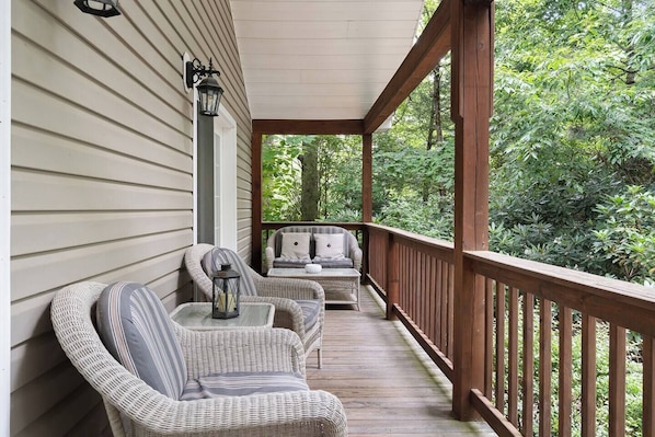 A covered porch with wicker furniture, a lantern, and a view of a wooded area.
