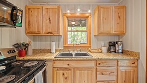A kitchen with wooden cabinets, a granite countertop, a stove, a sink, and a window with a view of greenery.
