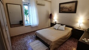 A neatly arranged bedroom with a bed, a bedside table with a lamp, a mirror, and a window with curtains. - Philoxenia Accommodation ~ Ralia's House (Κως)