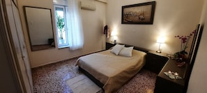 Ein ordentlich eingerichtetes Schlafzimmer mit Bett, Nachttisch mit Lampe, Spiegel und einem Fenster mit Vorhängen.