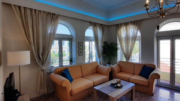 A living room with two sofas, a coffee table, a lamp, and large windows with curtains. - Philoxenia Accommodation ~ Ralia's House (Κως)