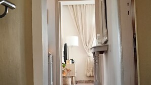 A hallway with a marble floor leading to a room with a bed, curtains, and a television. - Philoxenia Accommodation ~ Ralia's House (Κως)