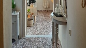 A hallway with a tiled floor, a white console table with a mirror, and a door leading to a room with a bed and curtains. - Philoxenia Accommodation ~ Ralia's House (Κως)