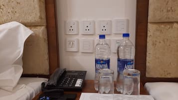 A hotel room with a bed, a bedside table with a phone, remote controls, and two bottles of Aquafina water.
