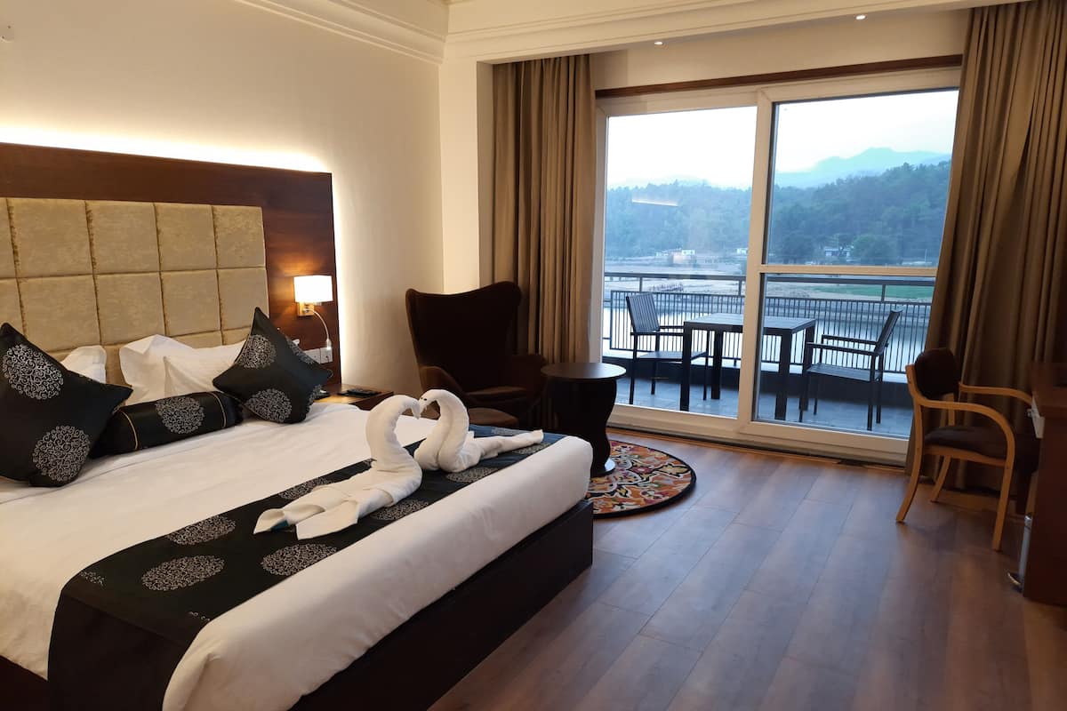 A hotel room with a large bed, a chair, a small table, and a balcony with a view of the mountains.