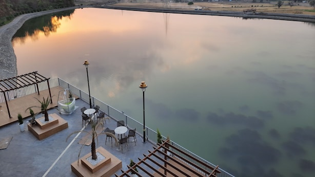 A serene riverside view with a wooden deck, outdoor seating, and a clear sky. - Jay Clarks Exotica (Nahan)