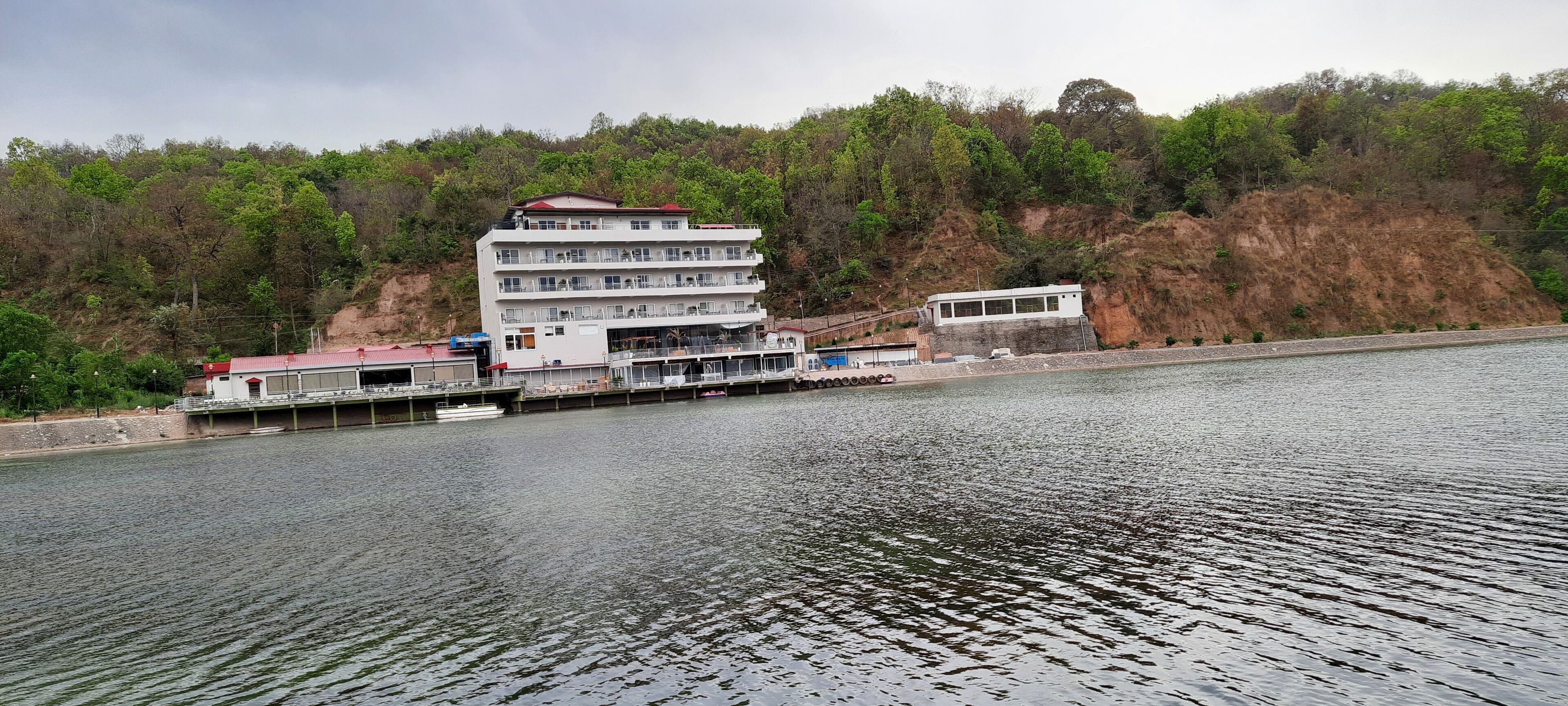 A waterfront hotel with multiple floors, a dock, and a hillside backdrop.