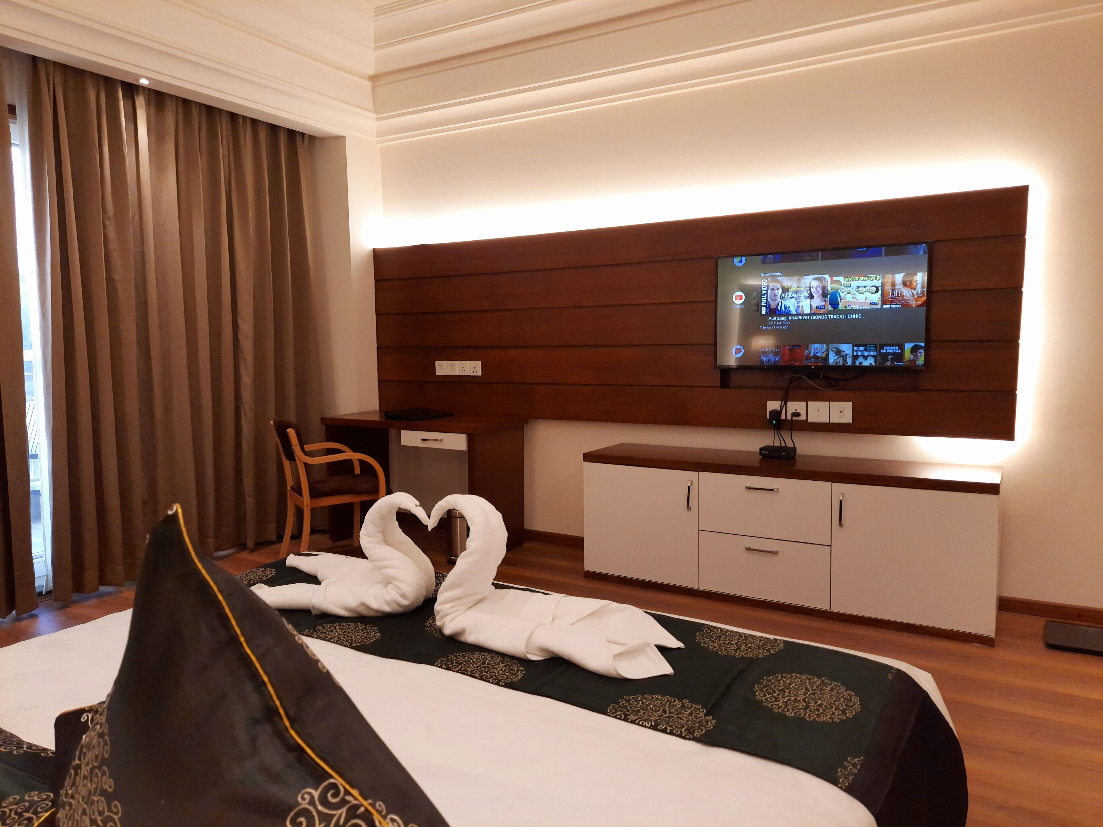 A hotel room with a bed, a TV mounted on the wall, a desk, and a chair.