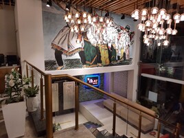 Una escalera con barandilla, un mural de personas con vestimenta tradicional y un letrero de neón que dice 'TLA'S'.