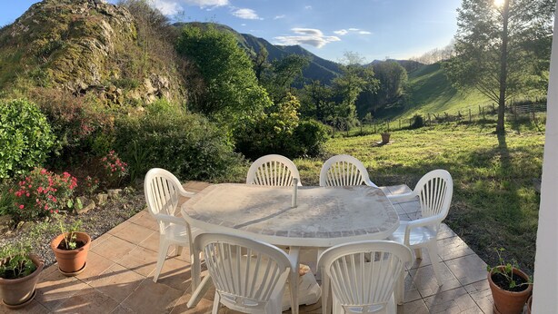 Een terras met een ronde tafel en witte stoelen, omringd door potplanten en uitzicht op een bergachtig landschap.