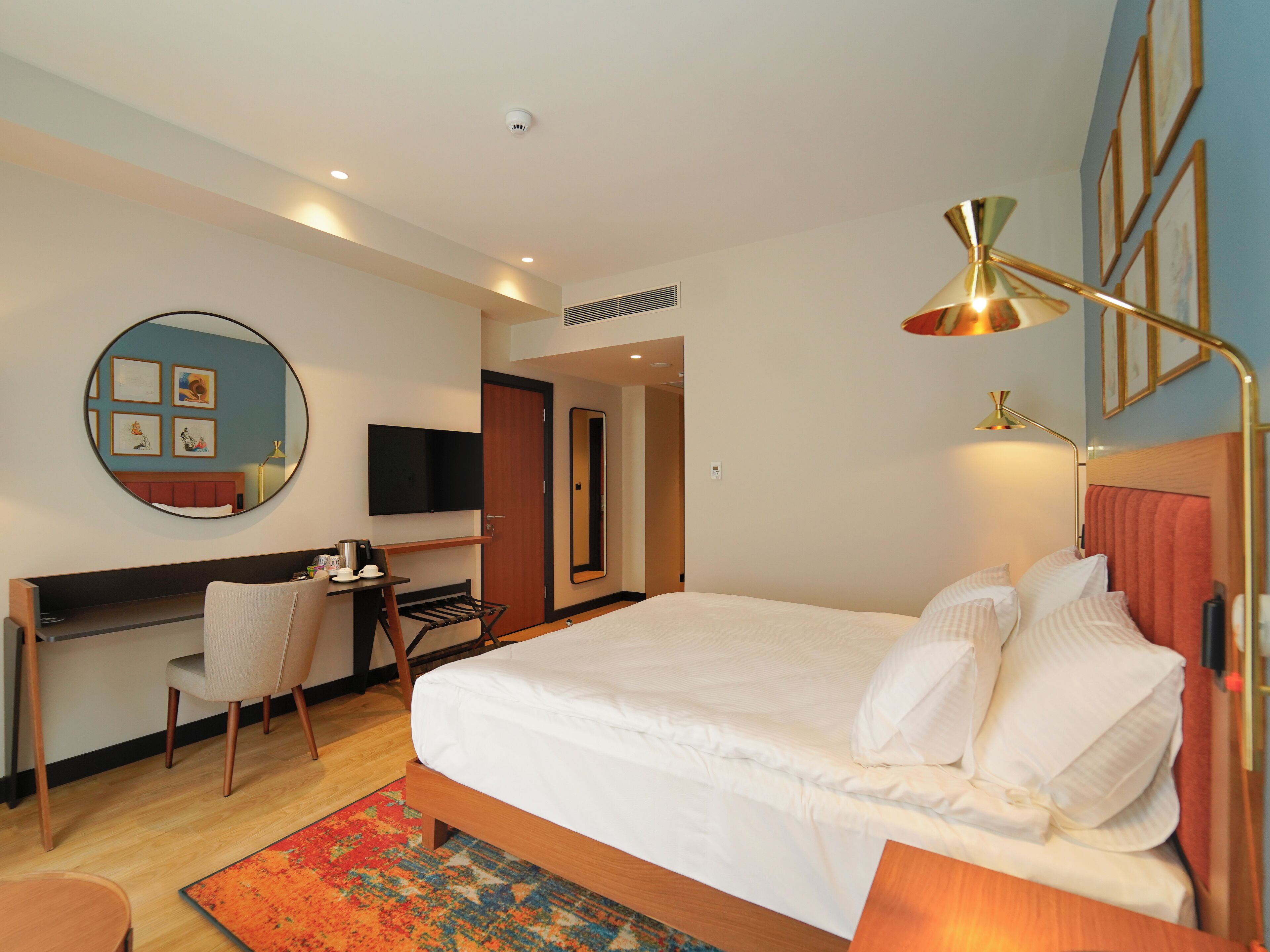 A hotel room with a bed, a desk, a chair, a TV, and a mirror.