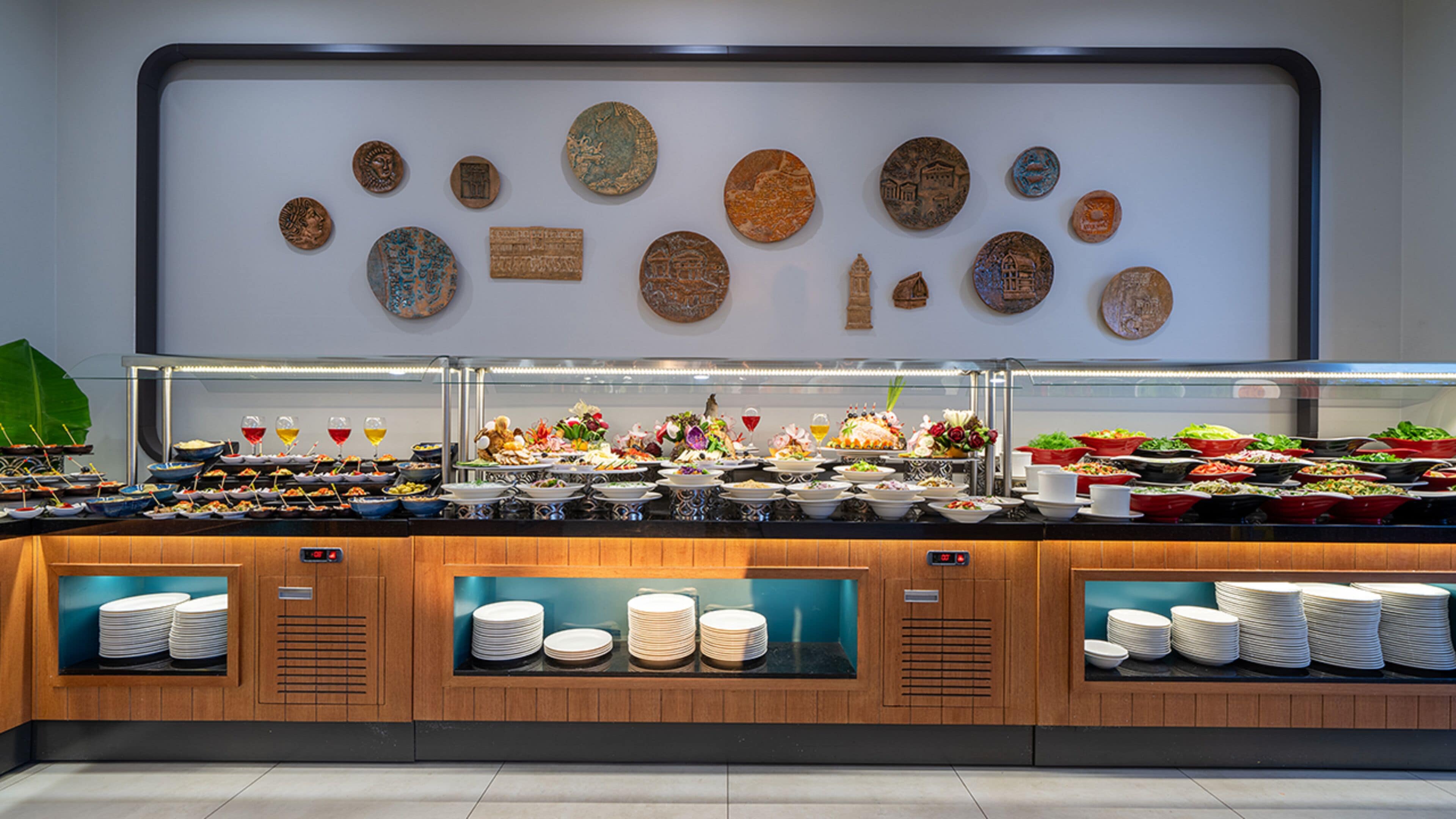 A buffet area with various food stations and a wall of decorative plates.