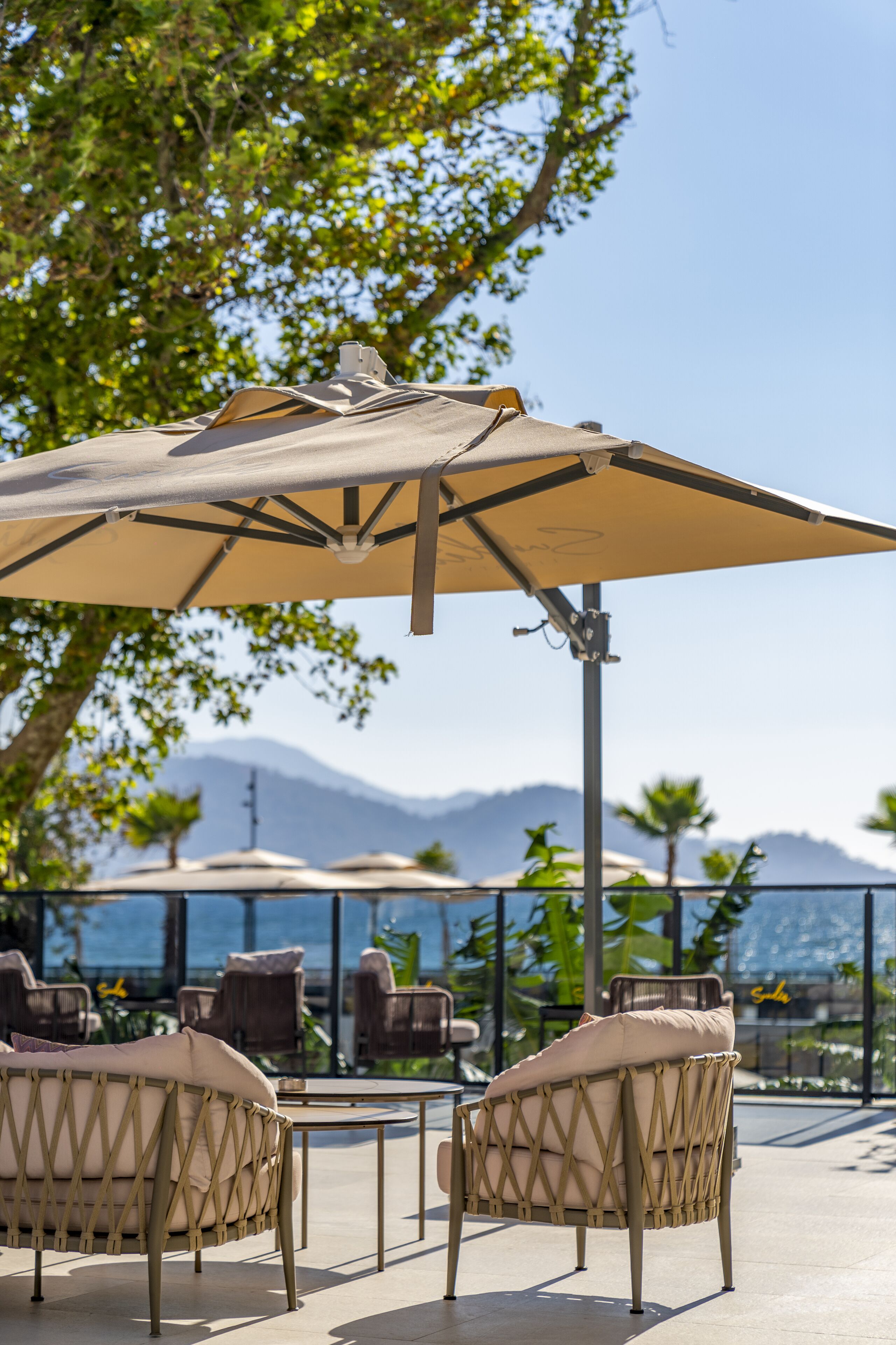 Outdoor seating with umbrellas, a view of the sea, and mountains in the background.