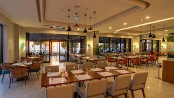 A spacious restaurant with multiple dining areas, large windows, and modern pendant lighting.