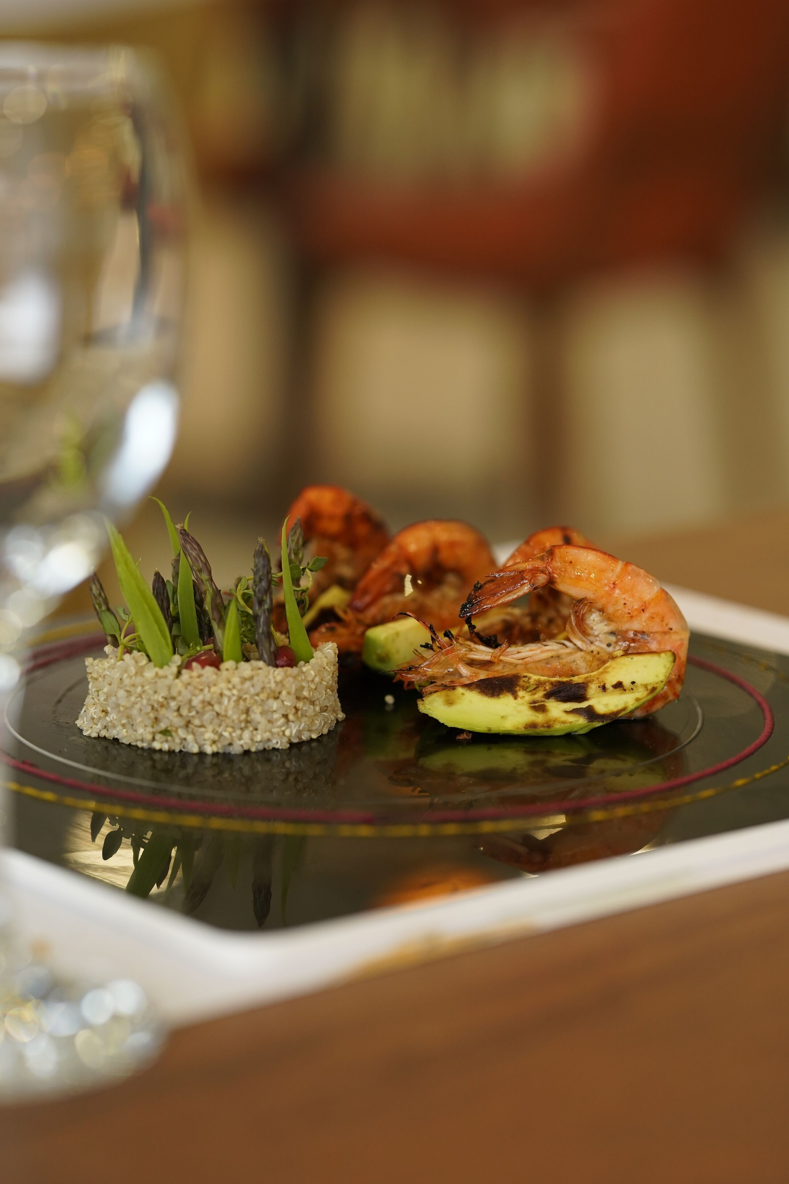 Une assiette noire bordée de rouge, sur laquelle sont disposées des crevettes grillées et des asperges.