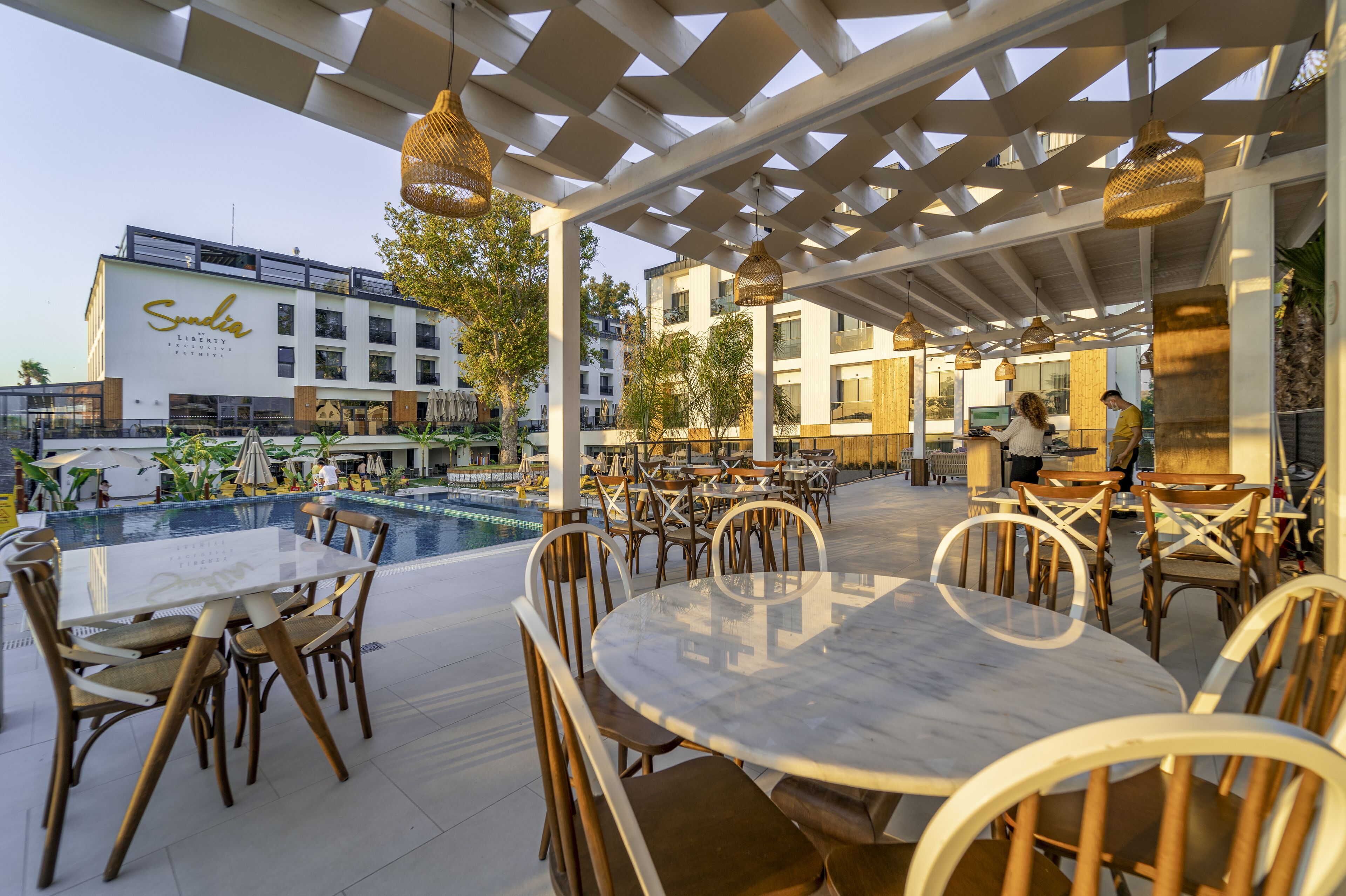 An outdoor dining area with tables and chairs, a pool, and a building with a sign.